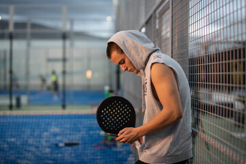 Young man with urban style takes a break with the phone trains after playing paddle tennis on an outdoor court