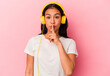Young Venezuelan woman listening to music isolated on pink background keeping a secret or asking for silence.
