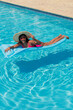 © Hector Pertuz - Young smiling African American girl in bikini, wearing straw hat relaxing on inflatable in swimming pool.