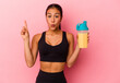 Young Venezuelan woman drinking a protein shake isolated on pink background having some great idea, concept of creativity.
