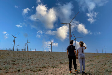 Wall Mural - A boy and a girl hold hands and look at the wind turbine. Concept Children look to the future