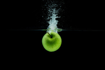 Wall Mural - Green apple falling in water with splash on black background.