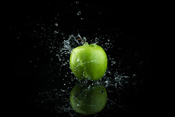 Green apple falling in water with splash on black background.