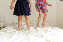 Close-up Of The Legs Of Two Young Girls Bouncing On A Bed