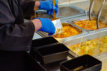 Wall Mural - Man holding a spatula serving food on an empty plastic food container in a cafeteria