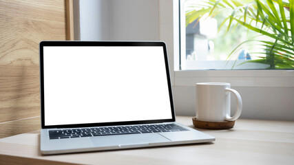 Close up view mock up laptop and coffee cup on wooden desk in living room.