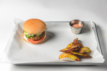 Bacon burger with beef patty, fresh tomatoes and cucumbers with sauce served on a metal tray over white background.