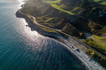 Wall Mural - Causeway Coastal Route a.k.a Antrim Coast Road A2 on the Atlantic coast in Northern Ireland. One of the most scenic coastal roads in Europe. Aerial view against the rising sun in winter