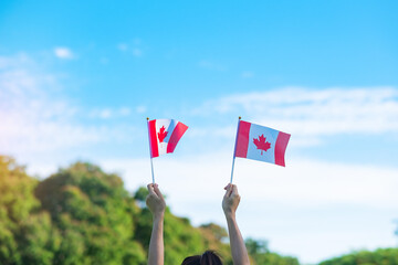 Wall Mural - hand holding Canada flag on blue sky background. Canada Day  and happy celebration concepts