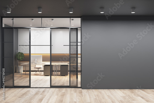 Black wall with copyspace for your text or logo next to doors to sunny office with monochrome style interior design, modern laptops on white tables and wooden floor. 3D rendering, mockup
