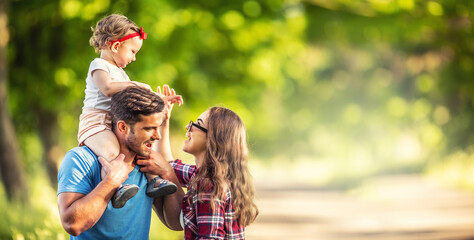 Happy family, father, mother and daughter are playing in the park and enjoying a sunny summer day