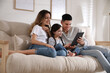 © New Africa - Happy family with little daughter using tablet on sofa in living room