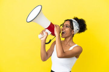 young african american woman isolated on yellow background shouting through a megaphone to announce 
