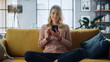 © Gorodenkoff - Beautiful Caucasian Female Using Smartphone in Stylish Living Room while Sitting on a Cozy Couch Sofa. Young Woman Resting at Home, Browsing Internet, Using Social Networks, Having Fun in Flat.