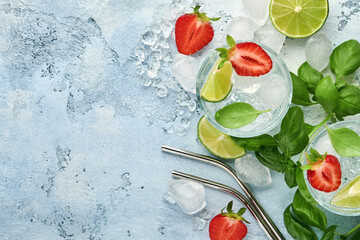 Two glasses of punch and fresh ingredients for making lemonade, infused detox water or cocktail. Strawberries, lime, mint, basil, ice cubes and shaker on grey stone or concrete background. Top view.