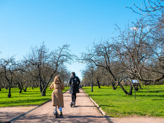 Bright sunny spring day in Kolomenskoye park, Moscow. People ride an electric scooter on a track in a large park and enjoy the good weather on a May day.