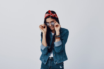 Wall Mural - Attractive young woman in bandana adjusting eyewear and smiling while standing against grey background