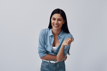 Wall Mural - Attractive young woman looking at camera and laughing while standing against grey background