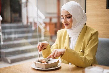 Wall Mural - Young muslim woman in hijab having a lunch in cafe