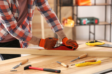 Wall Mural - Carpenter shaping wooden bar with hand plane at table in workshop, closeup