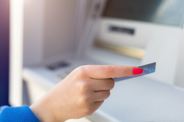 Female hand on a blurred background of an ATM machine with a card. Selective focus. Budget concept