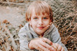 © Svetlana Glazkova - Portrait cute cool blonde caucasian Happy smiling little young boy in casual grey hoodie sitting in the tall grass against the backdrop of nature.