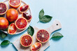 Composition of whole and sliced blood oranges in a plate on light blue table background. Flat lay, top view, close up