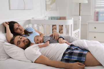 Wall Mural - Tired young parents with their baby sleeping in bed at home