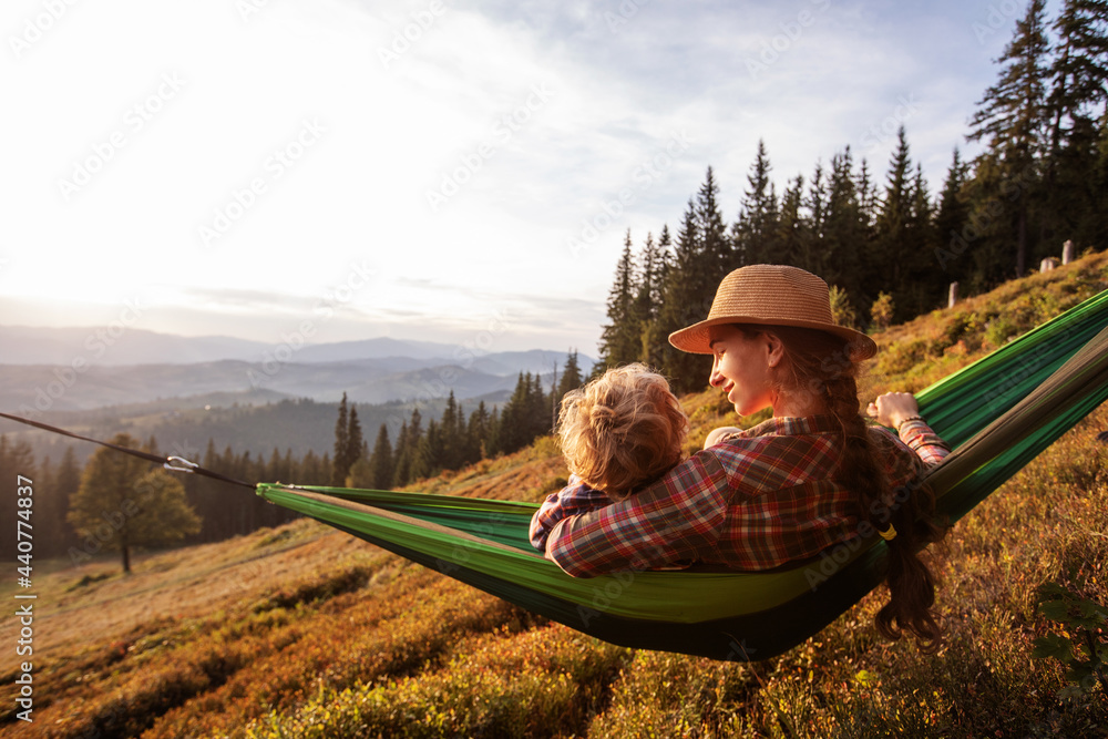 Boy with mom resting in a hammock in the mountains at sunset - obrazy, fototapety, plakaty 