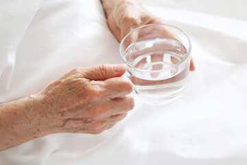 Elderly woman with glass of clean water in wrinkled hands. Concept of thirst, diet at retired, water purification, mineral drink