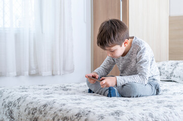 Little 6 years old boy using and playing on smarphone. Cute little boy playing games on smartphone in bed. Boy plays in video game on his smartphone. Social and technology concept.