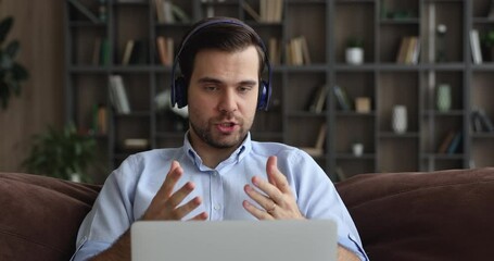 Wall Mural - serious man provide help to client via video call, wear headphones sit on sofa with laptop work from