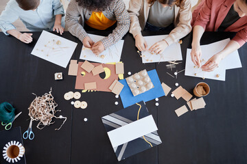 Top view at group of children making cardboard models during art and craft class in school with female teacher, copy space