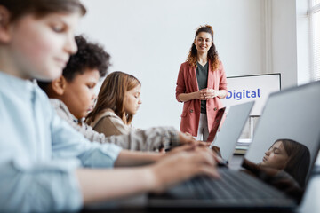 Wall Mural - Portrait of smiling female teacher with group of kids using computers during IT lesson in school