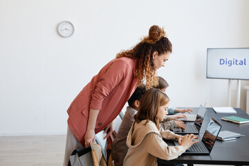 Wall Mural - Side view portrait of female teacher helping children using laptop during IT class in school, copy space