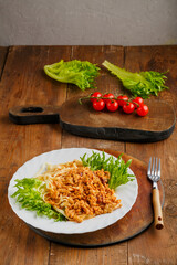 A plate of pasta in bolognese sauce on a nearby fork and cherry tomatoes on a board.