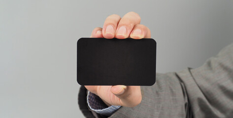 Hand is holding black blank card and wear suit on gray background. business man concept