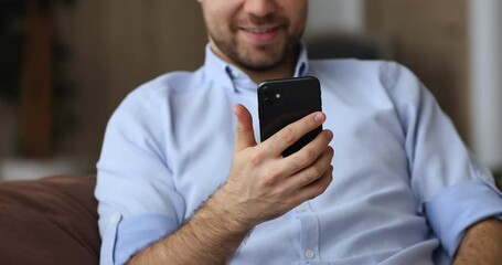 Sticker - Close up cropped view young smiling man sit on couch with smart phone device, texting message, send sms using modern wireless tech, e-commerce client purchasing via e-store mobile application concept