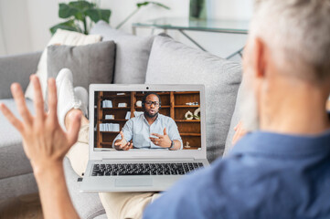 Two diverse male colleagues talking on the distance via video connection. Senior grey haired man greeting to African-American guy on the laptop screen. Mature student learning language online