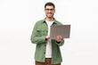 © Damir Khabirov - Young man standing in casual green shirt, holding laptop and looking at camera with happy smile, isolated on gray background
