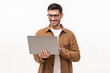 Young happy man standing with opened laptop, browsing online or typing message, isolated on gray background