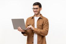 Young Stylish Man Wearing Casual Brown Shirt, Standing With Opened Laptop, Surfing Online Or Typing, Isolated On Gray Background