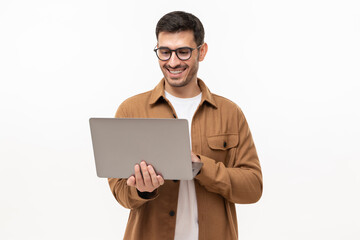 young happy man standing with opened laptop, browsing online or typing message, isolated on gray bac