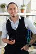 © DragonImages - Portrait of handsome smiling trader standing at his table with smartphone in hands and looking at camera when making phone call to client