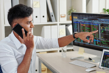 Wall Mural - trader pointing at computer screen with stock market data when talking on phone with client or colle