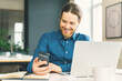 © Nata Bene - Smiling young guy employee in casual wear looking at smartphone screen, reading good news in message or chatting with friend in social media while working at workplace in modern office