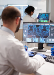 Wall Mural - man biologist checking dna informations typing on pc in modern equipped laboratory. group of biochem