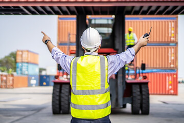 Rear view of engineer in reflective clothing with safety helmet is working and checking at containers cargo on shipping port area at harbor