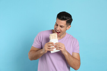 Man eating delicious shawarma on turquoise background