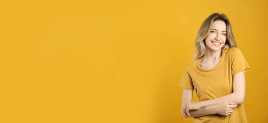 Poster - Portrait of happy young woman with beautiful blonde hair and charming smile on yellow background. Space for text